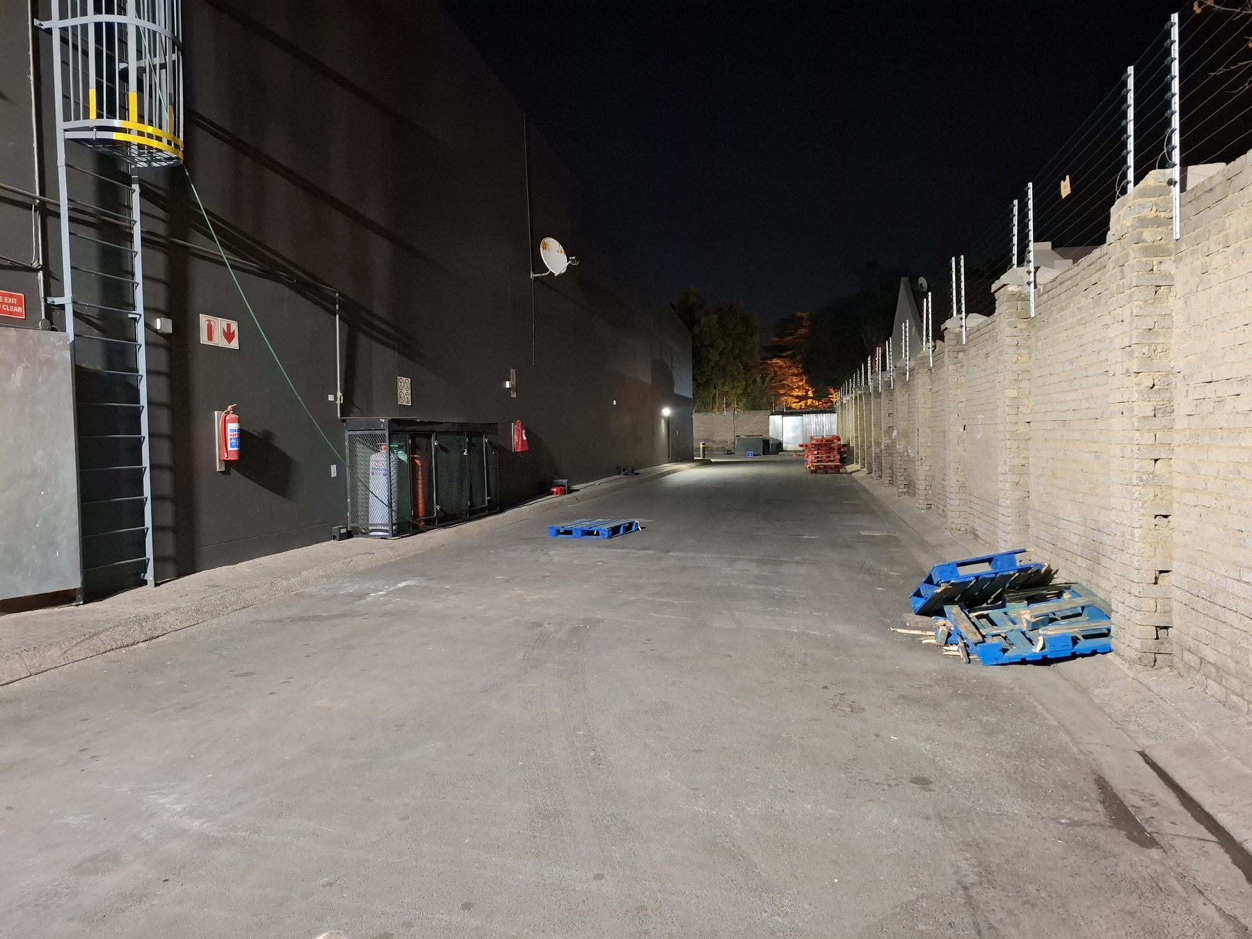 Boundary wall with electric fencing along the rear yard, lit at night